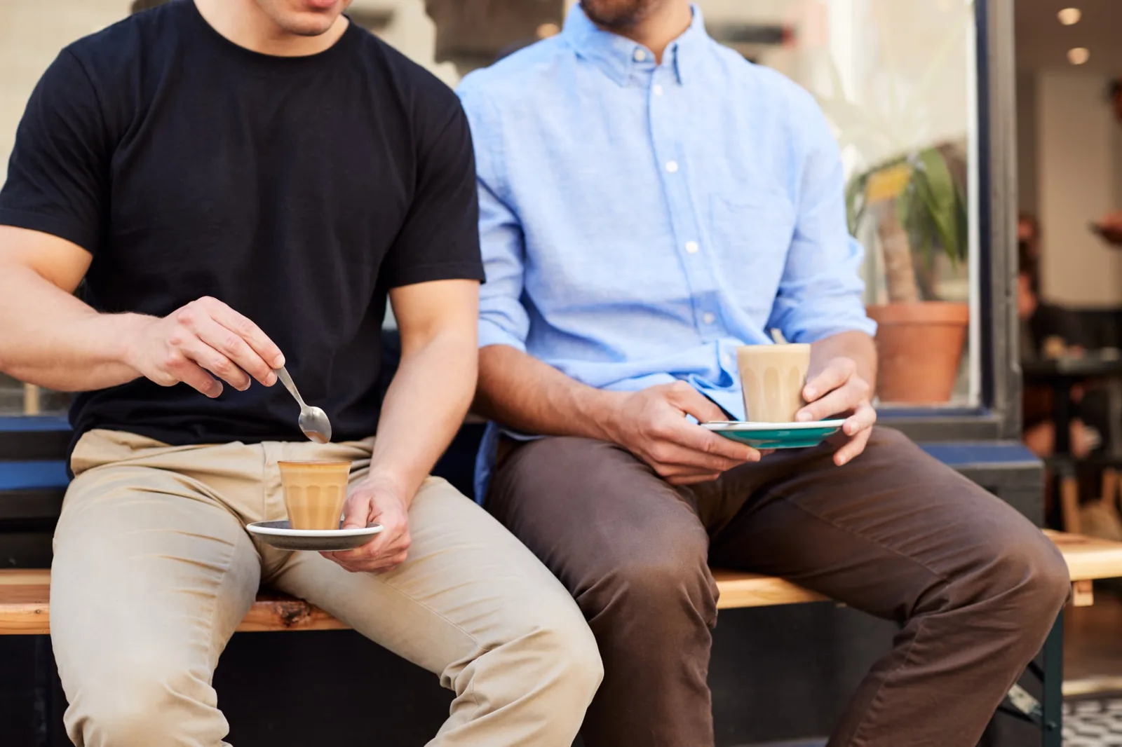 Two business owners on a bench outside a cafe, coffee in hand